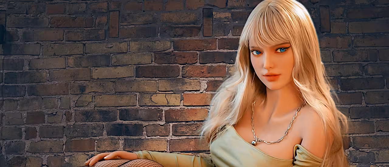 Poupée sexuelle blonde aux formes réalistes, assise devant un mur de briques. Cliquez pour voir toutes les poupées sexuelles.